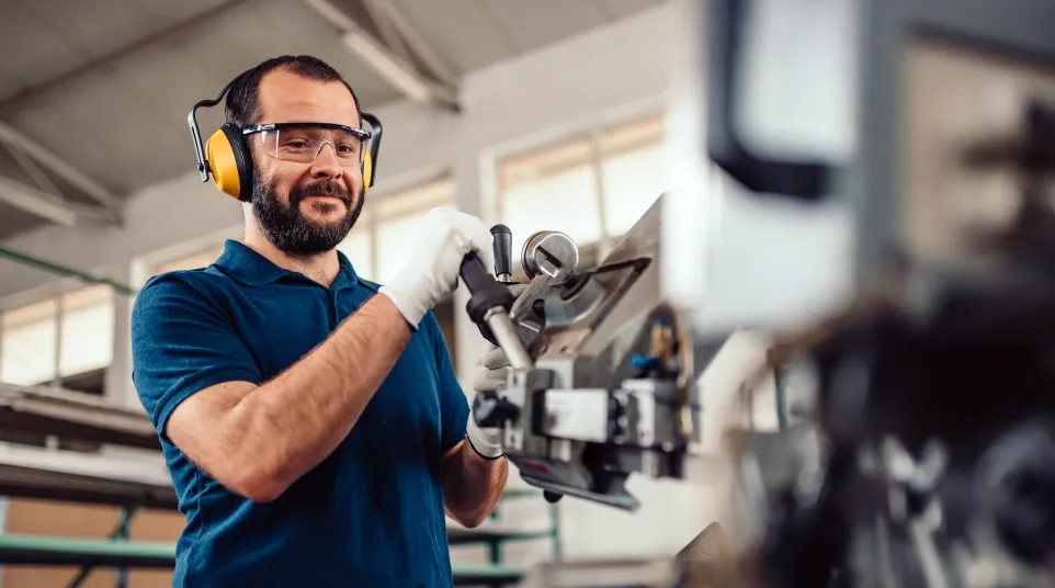 A skilled worker operating machinery in a manufacturing facility, wearing protective gear.
