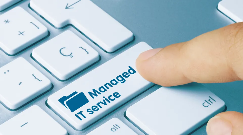 A hand pressing a keyboard key labeled 'Managed IT Service' on a laptop.