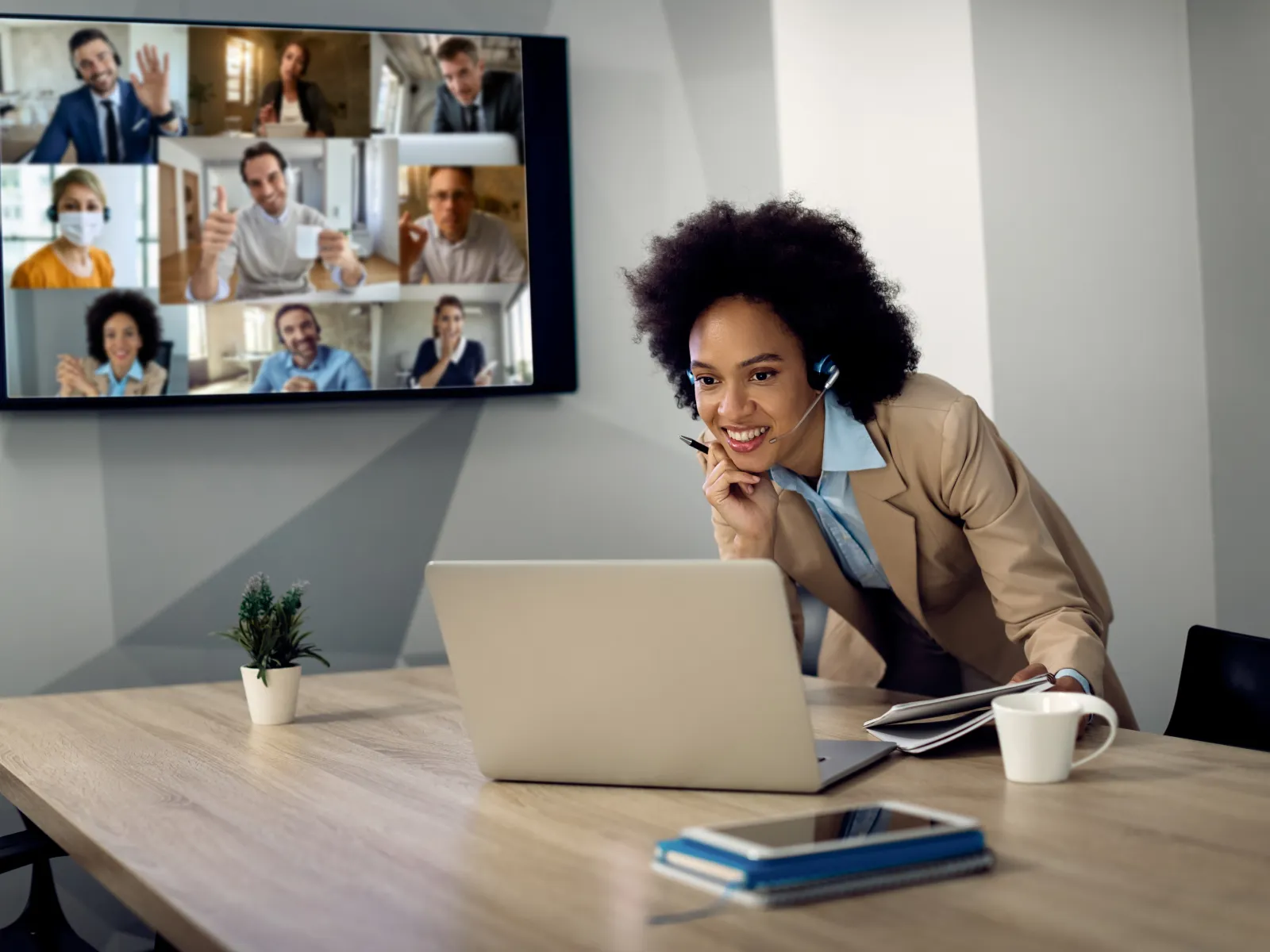 Young professional woman with headset engaging in a video conference with nine colleagues on a large screen